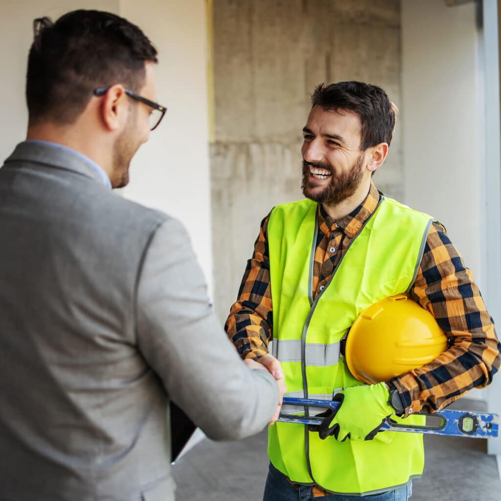 Smiling construction worker shaking hands with supervisor while standing in building in construction process.